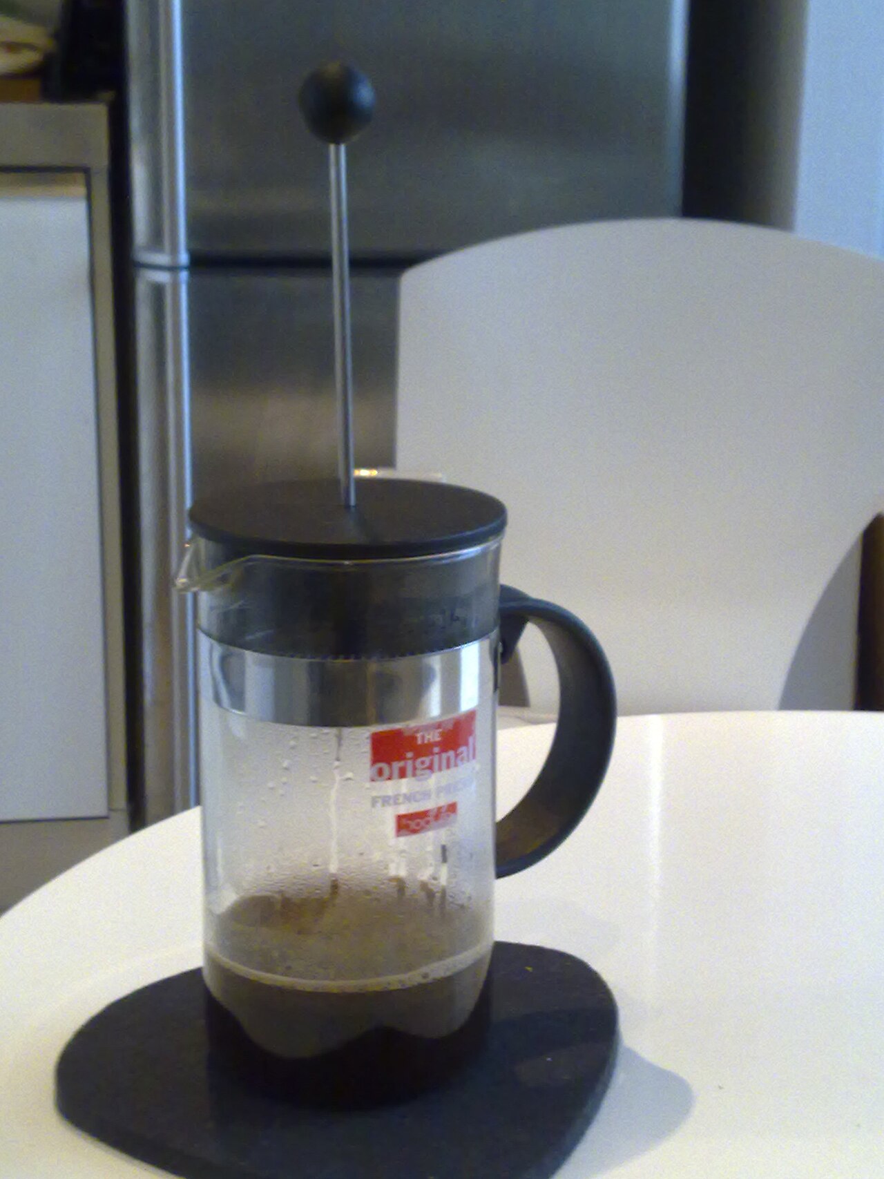 Close-up shot of a Bodum Chambord French press plunger descending into dark coffee, steam rising.
