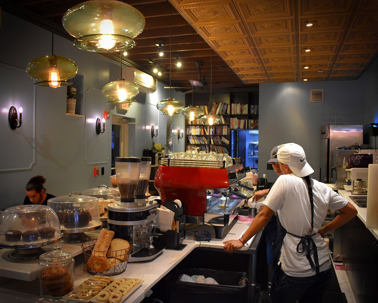 A close-up of small plastic cups of Cuban coffee being served through a walk-up window (ventanita) with hands exchanging money.